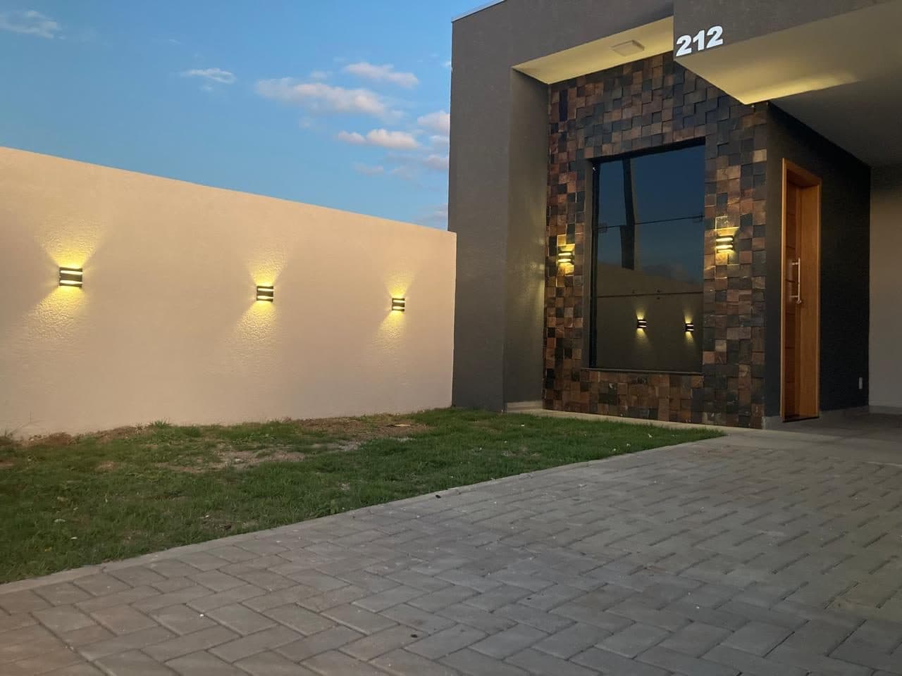 Entrada de casa do Vila Marly ao anoitecer, com fachada em pedra natural e arandelas acesas